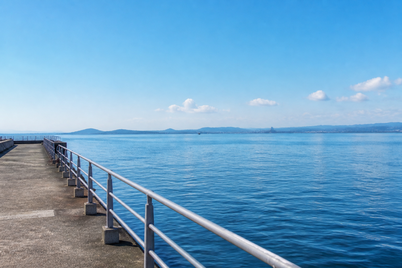 青空の下で護岸から海を臨む釣り場の風景と穏やかな潮の流れ